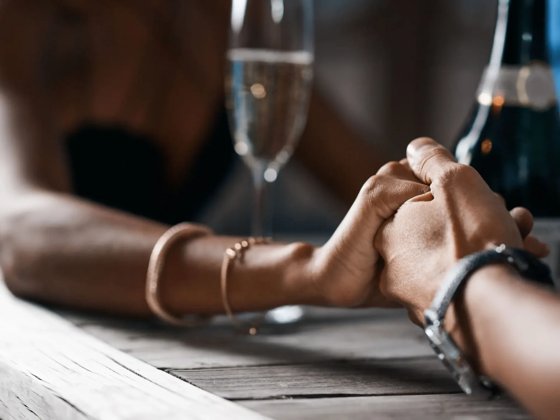 Couple holding hands across a table with a glass of champagne.